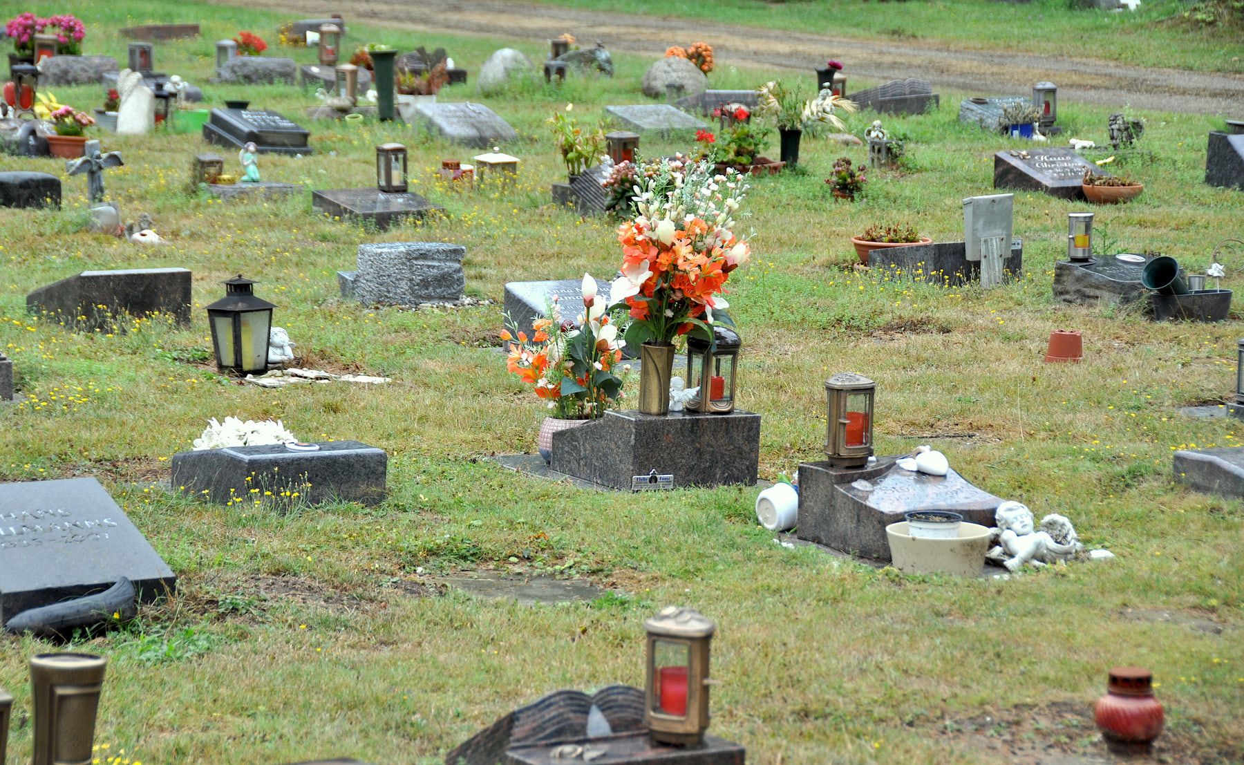 Weites Rasengräberfeld mit niedrigen liegenden Grabsteinen, zahlreichen Laternen und orange-weißen Blumenarrangements auf Westfriedhof Köln