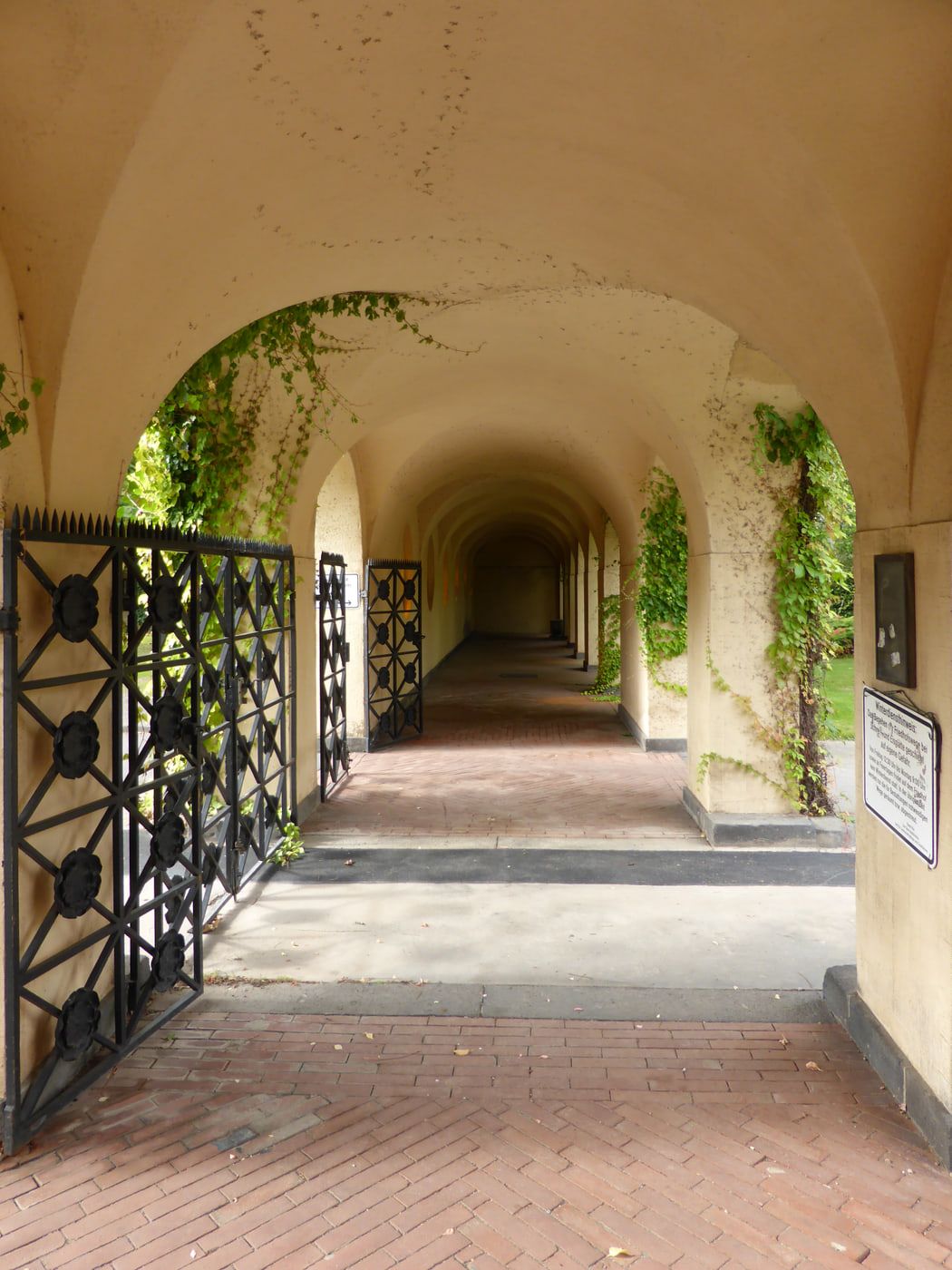 Langer gewölbter Laubengang am Haupteingang mit Efeu und Ziergittern auf Westfriedhof Köln